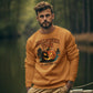 A man wears an orange Halloween Town sweatshirt with a pumpkin graphic and khaki pants.