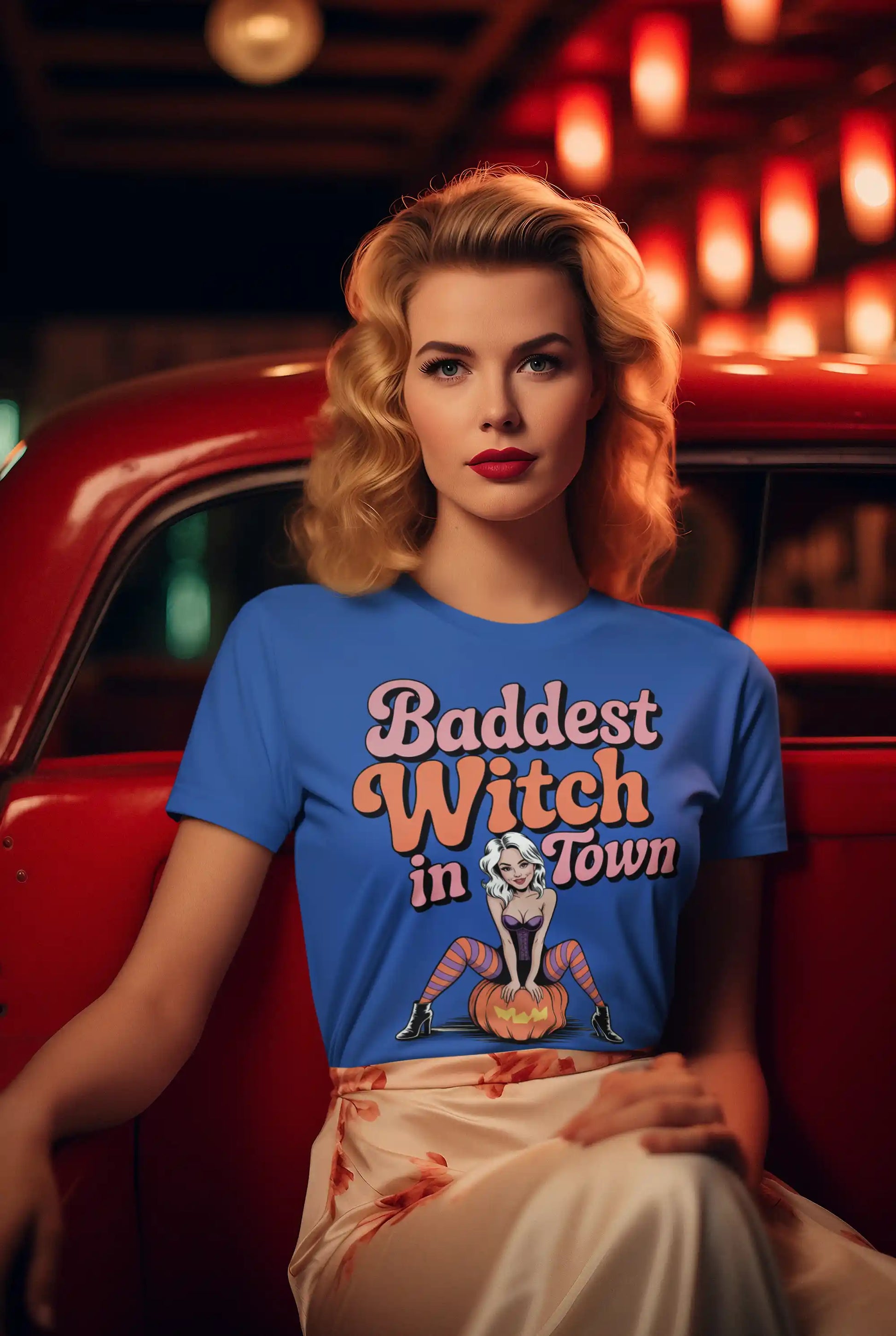 A woman in a blue "Baddest Witch in Town" t-shirt sits in a red car.
