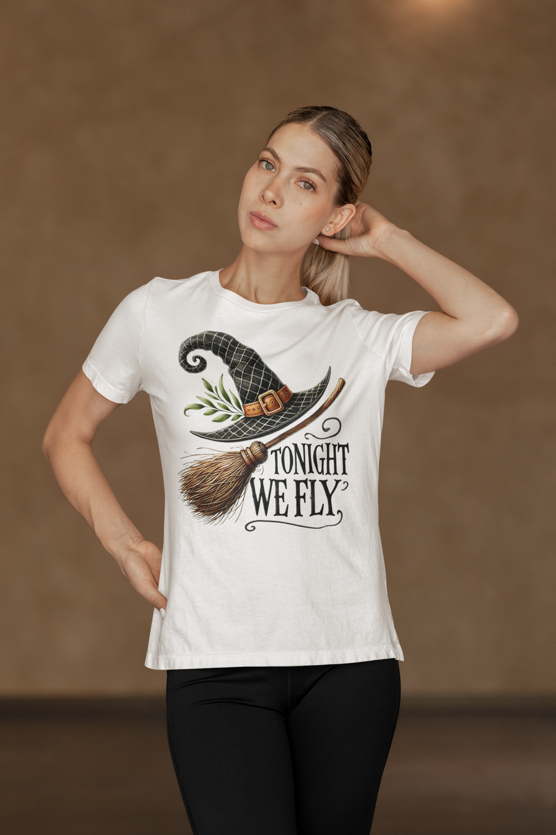A woman models a white t-shirt with a witch hat, broom, and "Tonight We Fly" graphic.