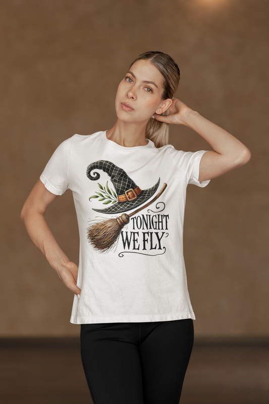 A woman models a white t-shirt with a witch hat, broom, and "Tonight We Fly" graphic.