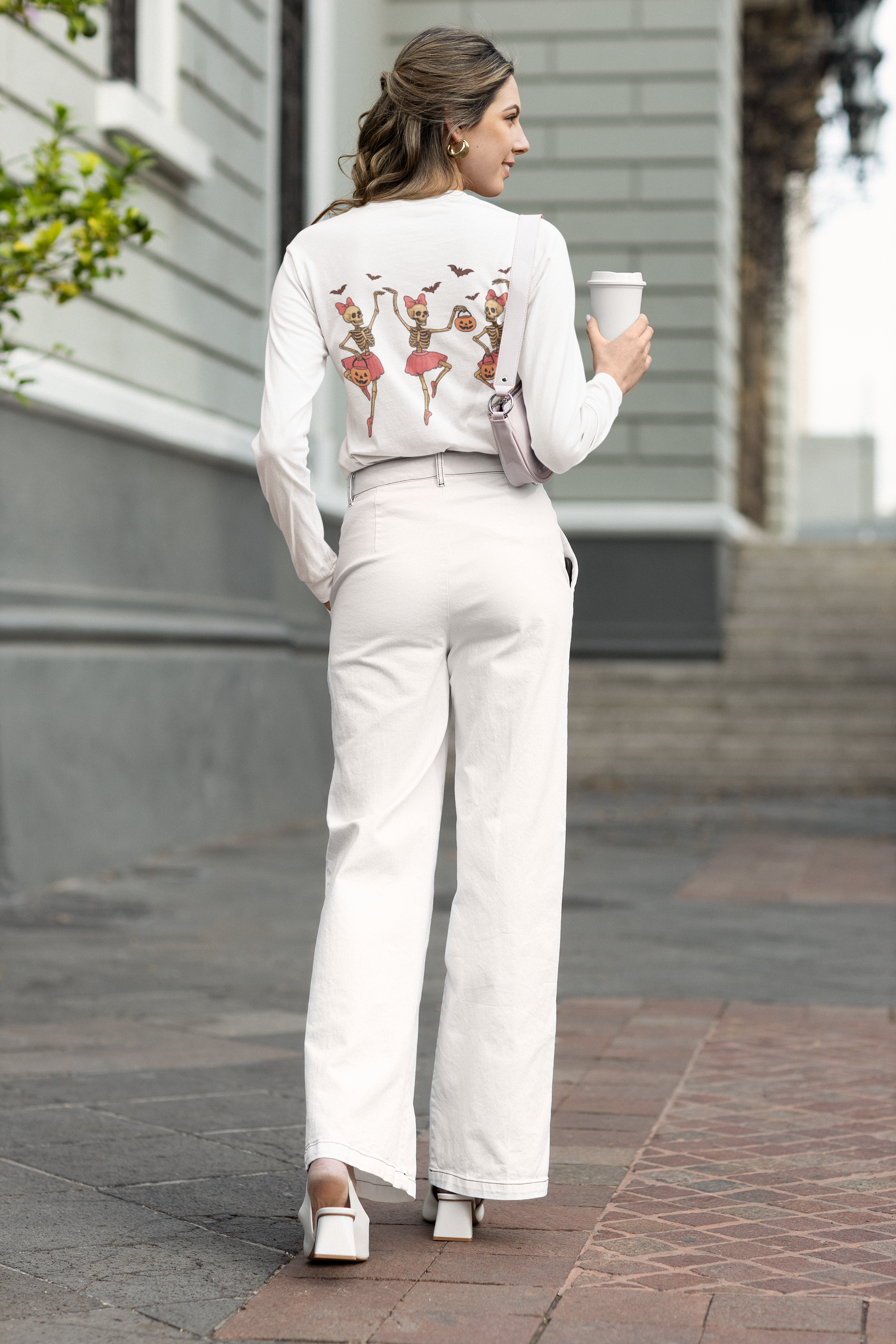 A woman wears a white long-sleeve shirt with dancing skeleton ballerinas on the back.