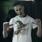 A man in zombie makeup points to a white t-shirt with a witch hat and broom.