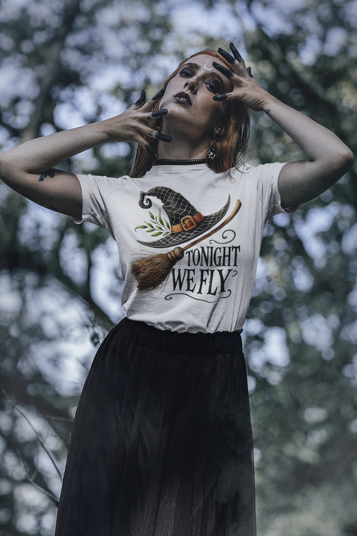 A woman wears a white t-shirt with a witch hat, broom, and "Tonight We Fly" graphic.