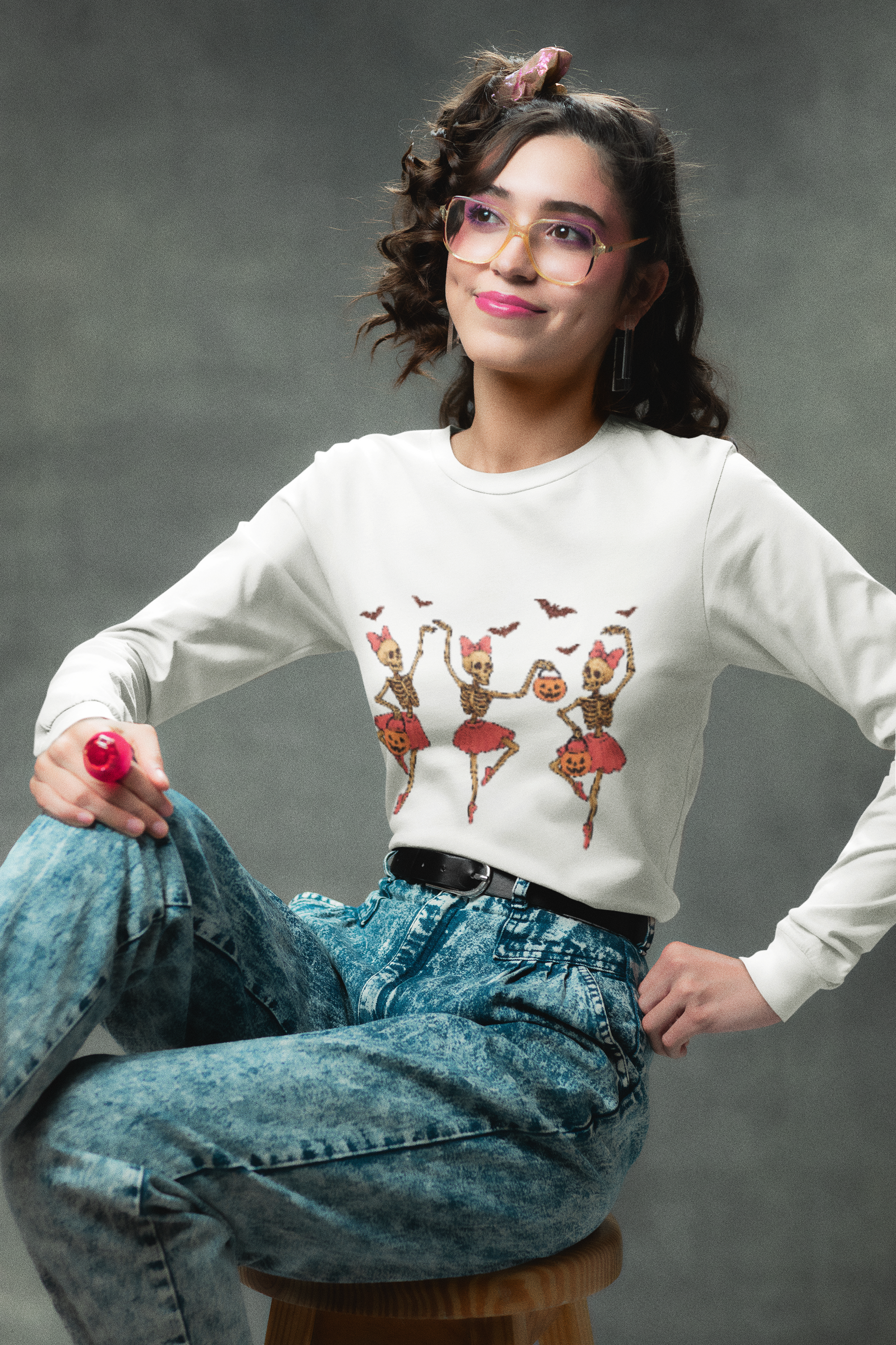 A woman in a white long-sleeve shirt with dancing skeletons and acid-wash jeans.