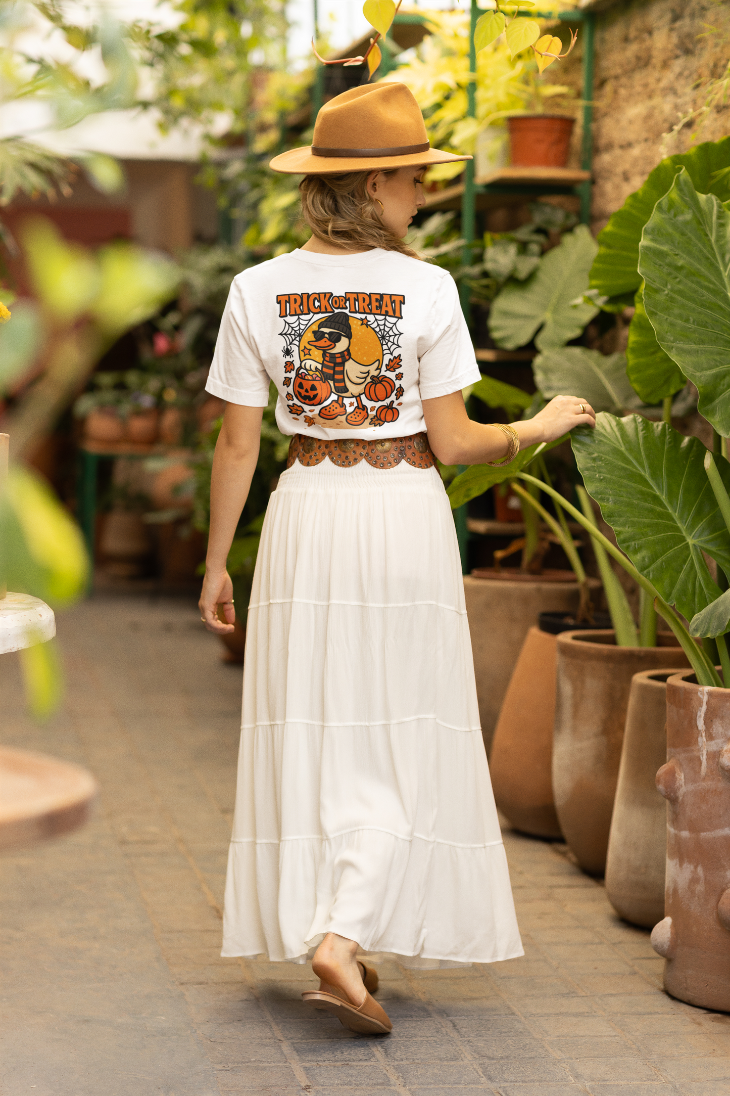 A woman from behind wears a white Halloween duck t-shirt, a long white skirt, and a brown hat.