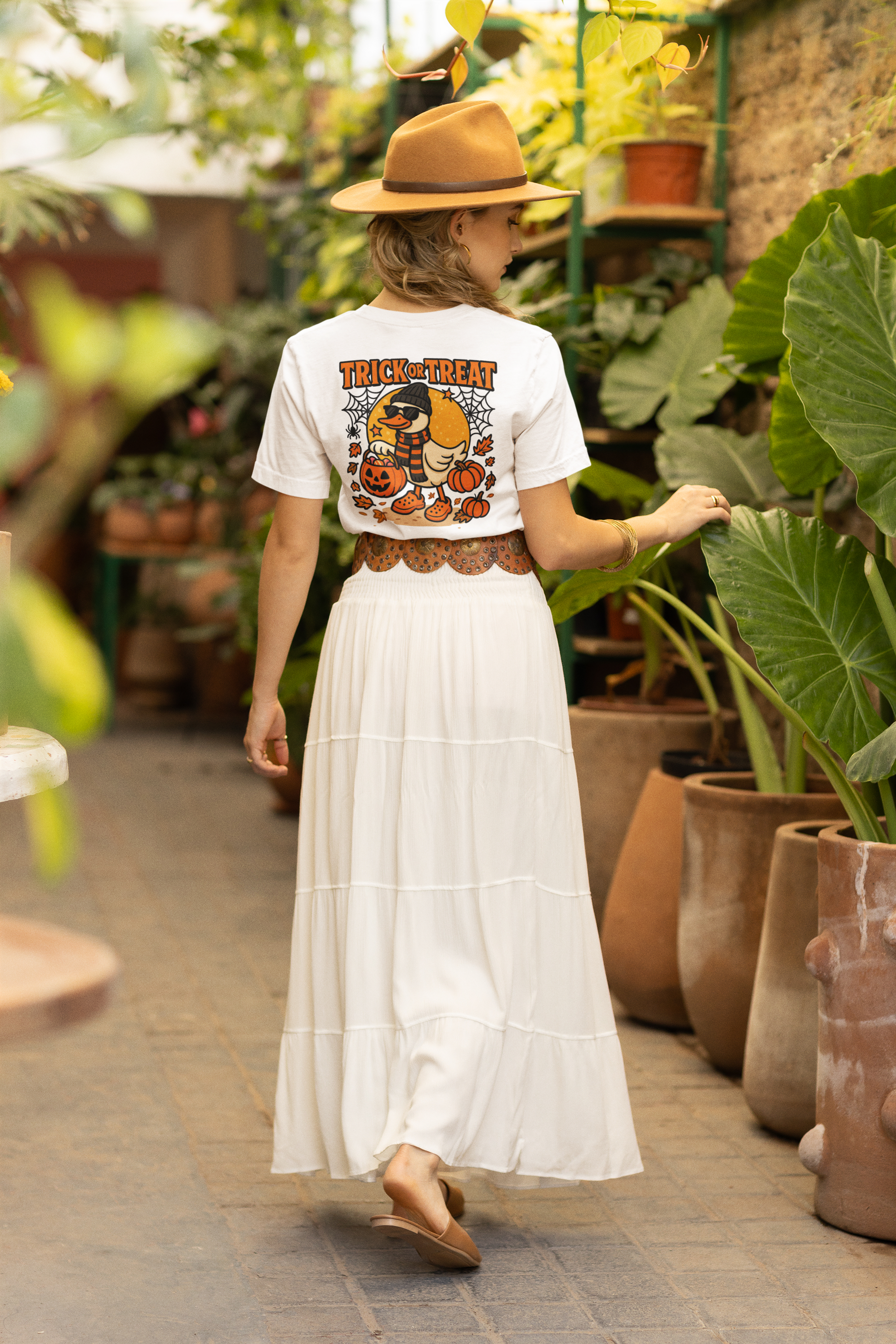 A woman from behind wears a white Halloween duck t-shirt, a long white skirt, and a brown hat.