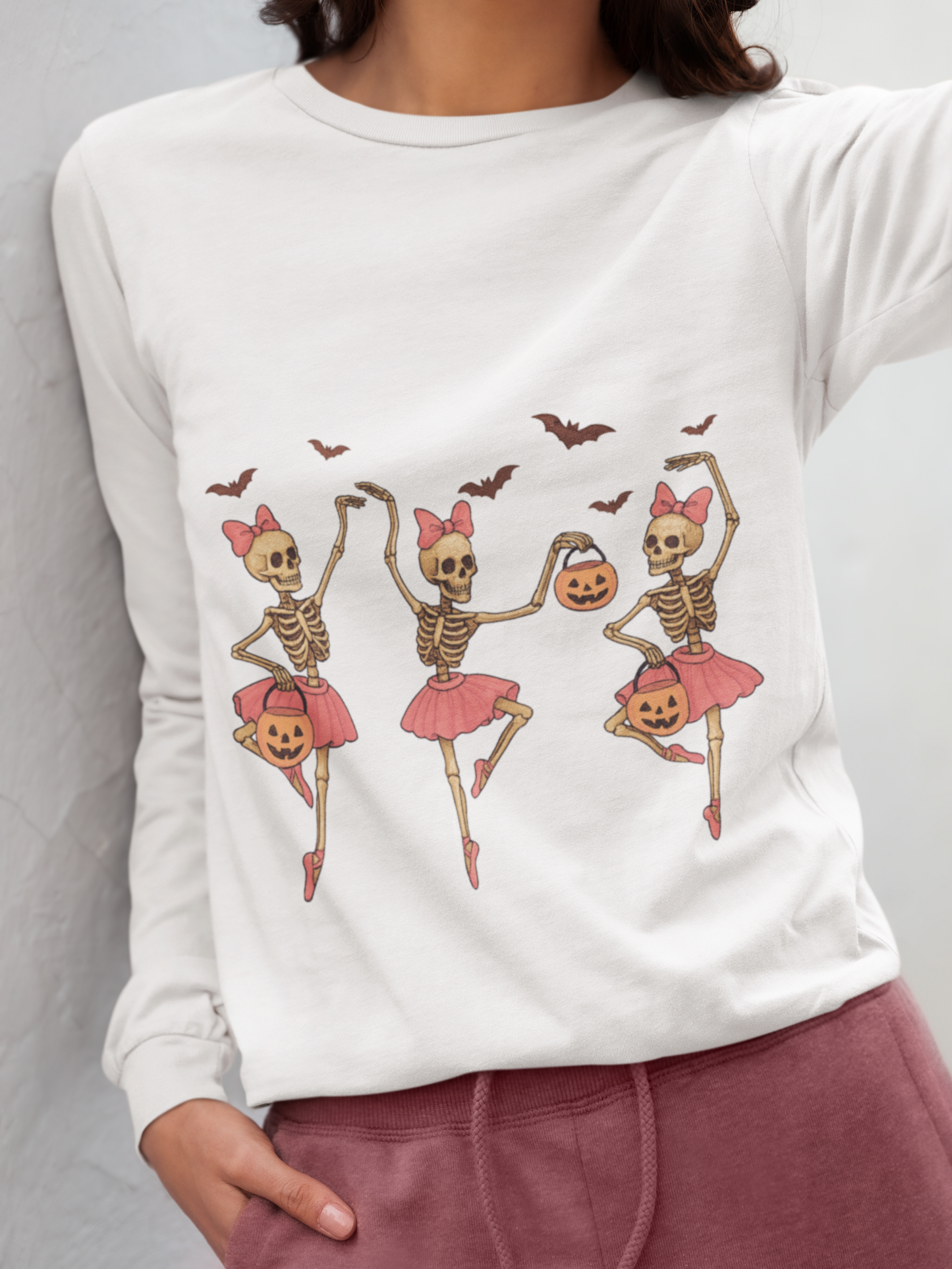 A person wears a white long-sleeve shirt with three dancing skeleton ballerinas.