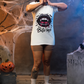 A woman in a white "Bite Me" vampire lips t-shirt stands in a Halloween setting.