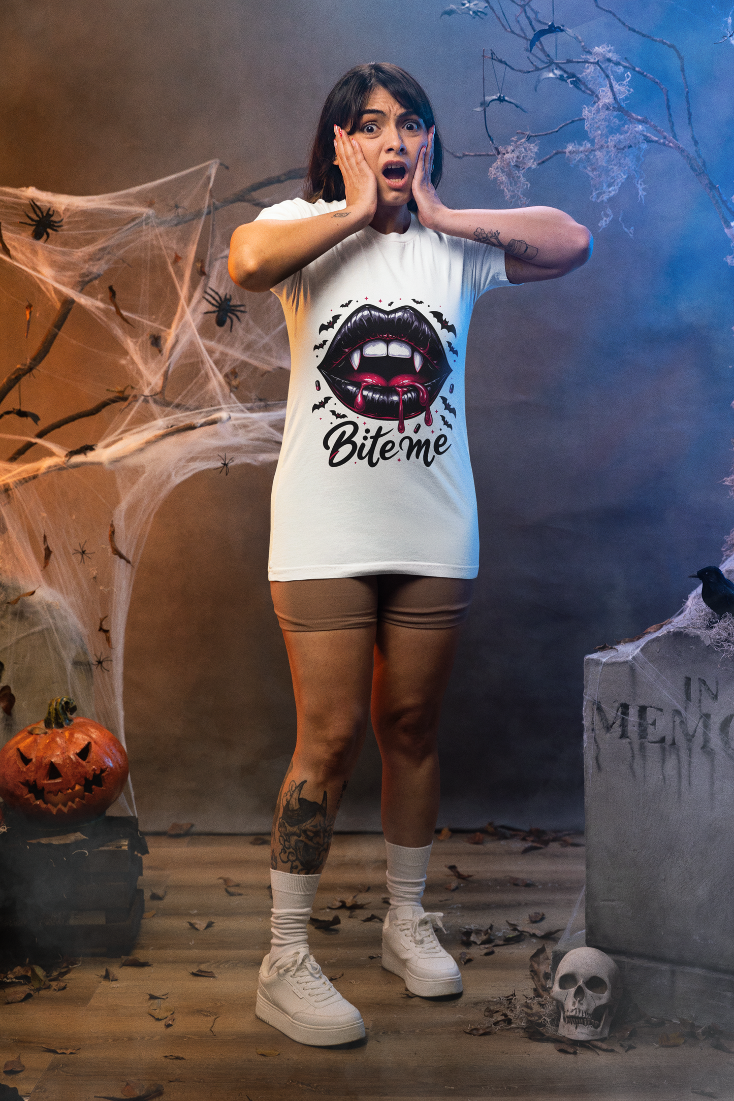 A woman in a white "Bite Me" vampire lips t-shirt stands in a Halloween setting.