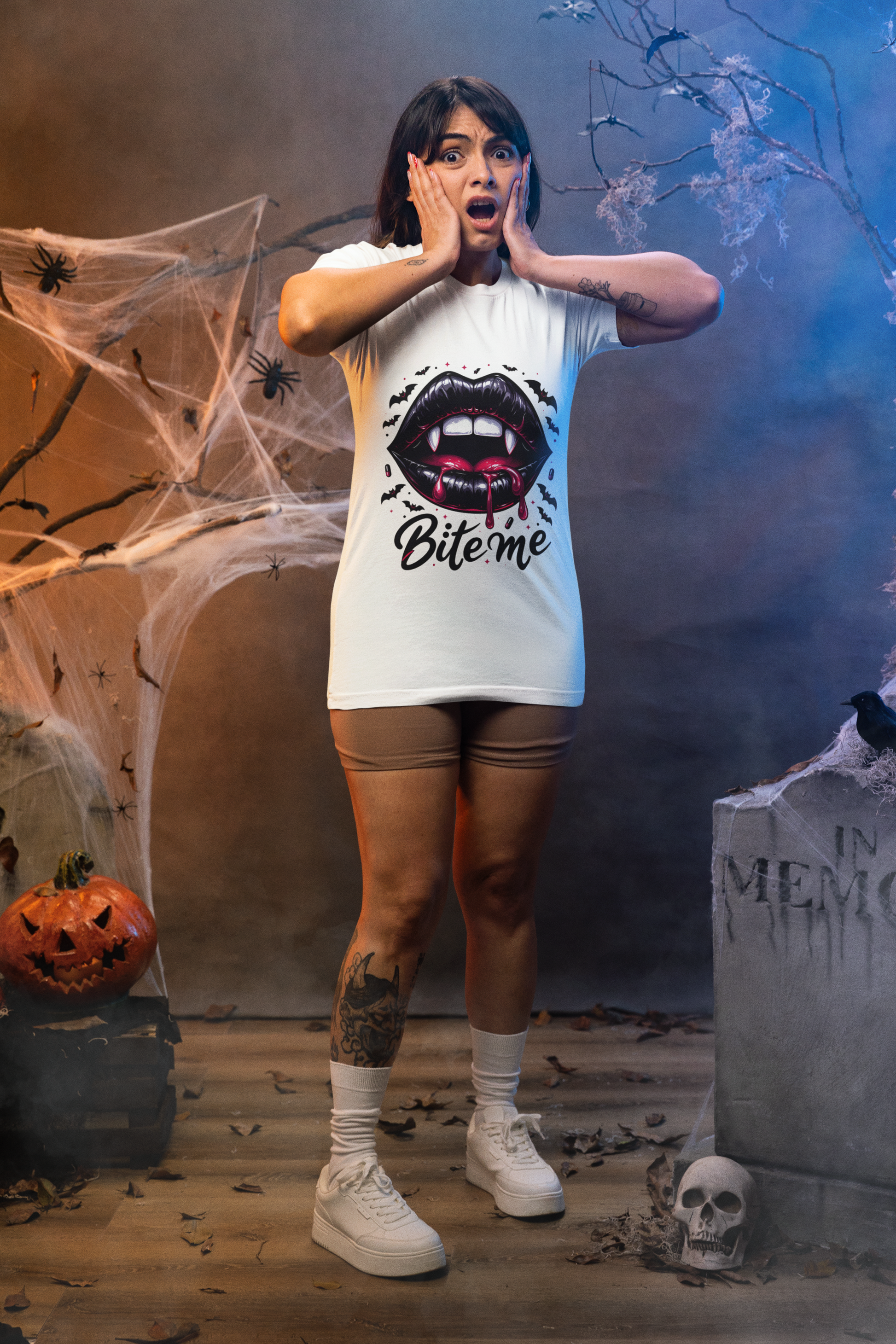A woman in a white "Bite Me" vampire lips t-shirt stands in a Halloween setting.