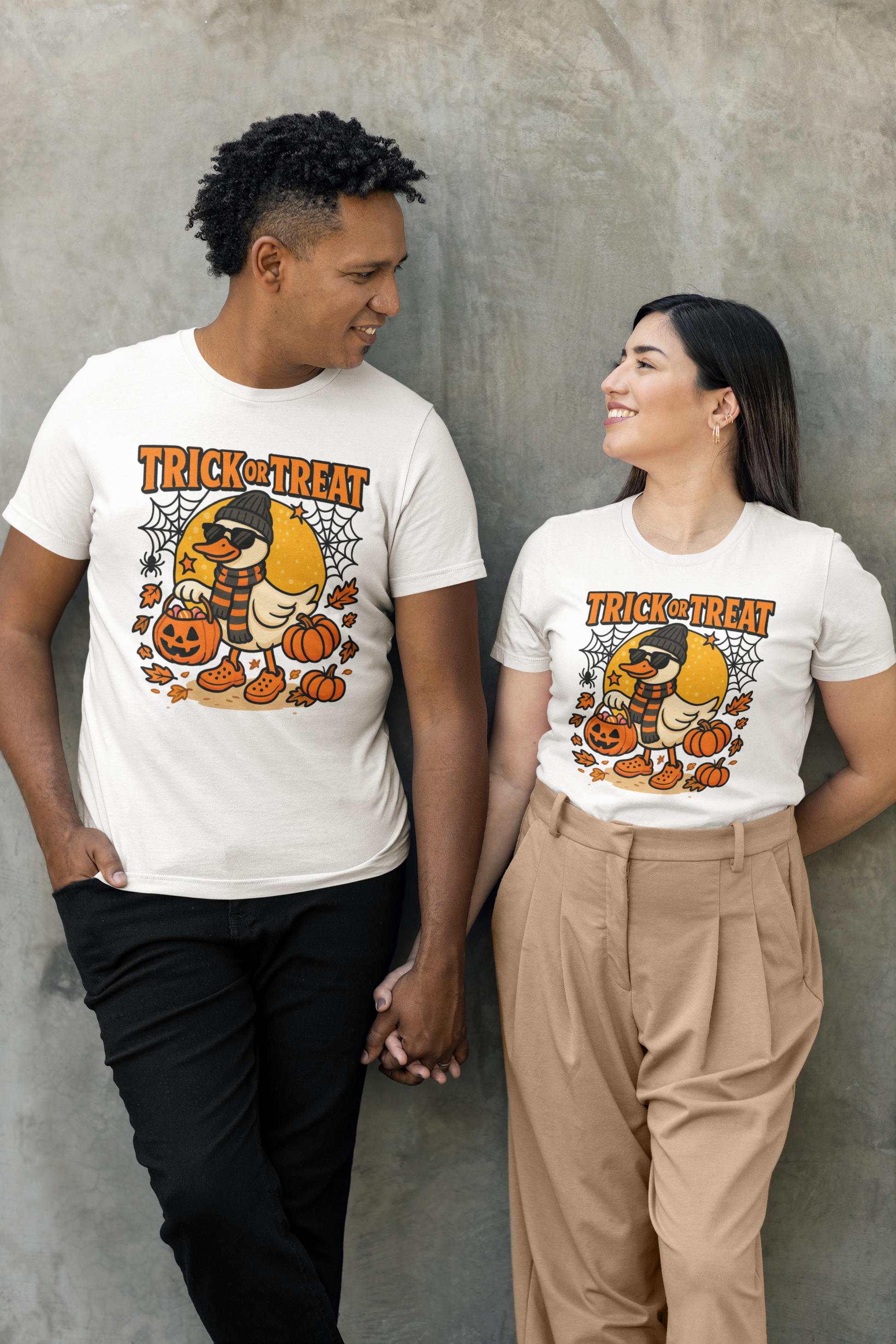 Two people wear white "Trick or Treat" t-shirts with a duck, pumpkins, and spiderwebs.