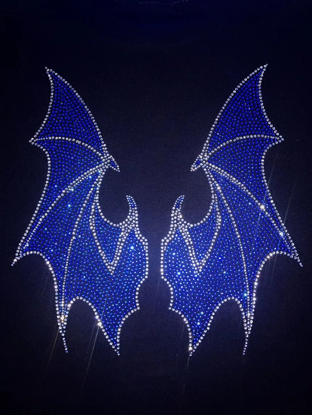 A black hoodie features two large, blue rhinestone bat wings on the back.