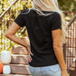 A woman from behind wears a black short-sleeve t-shirt and a light denim skirt.