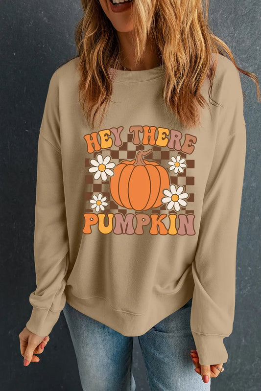 A woman wears a tan long-sleeve sweatshirt with a "Hey There Pumpkin" graphic.