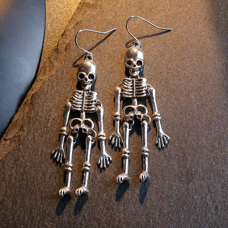 A pair of silver-colored skeleton alloy earrings are displayed on a dark surface.