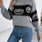 A woman wears a gray long-sleeve sweater with black pumpkin designs and blue jeans.