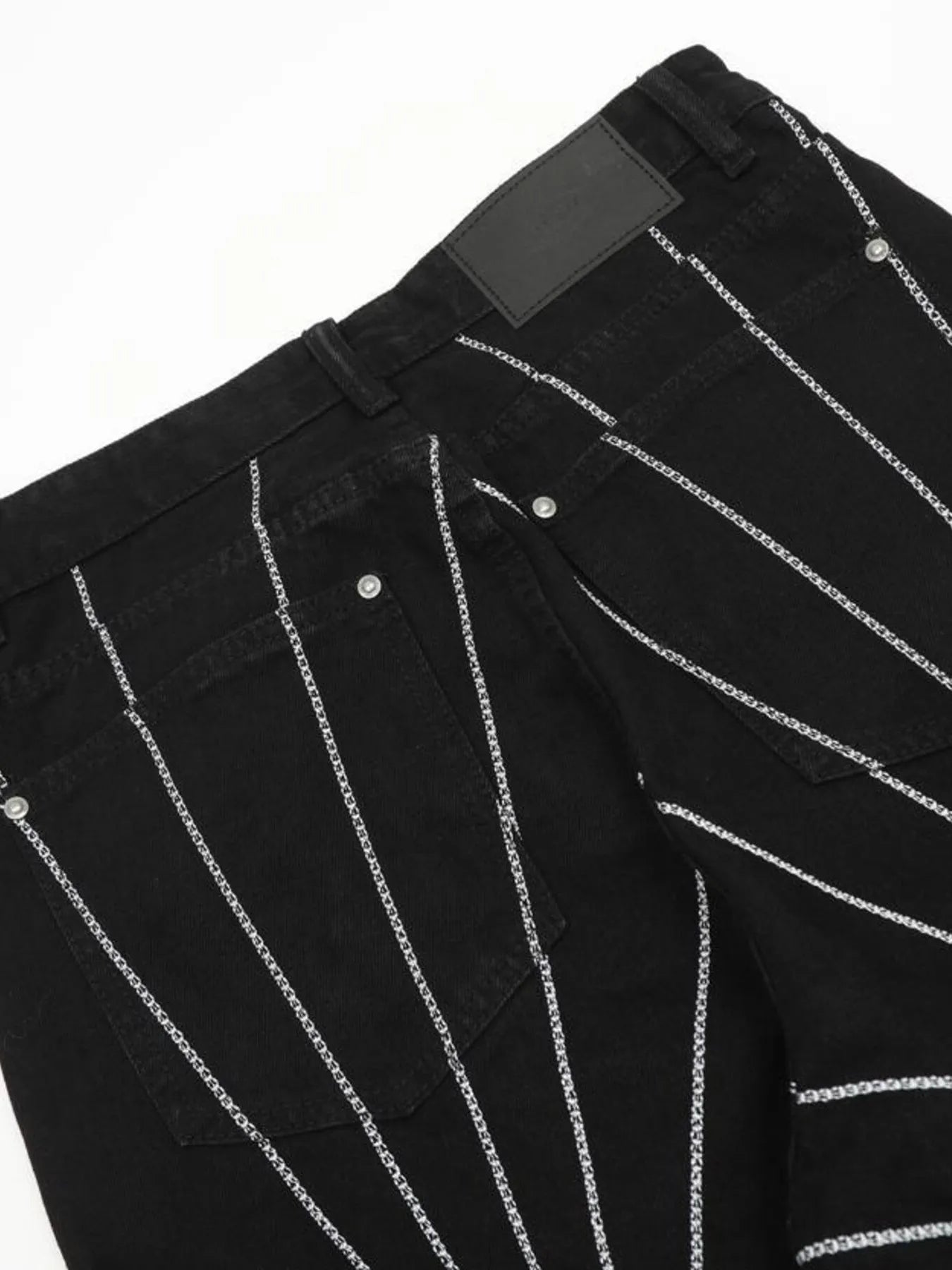 Men's black flared jeans with silver chain-like embroidery forming a spider web pattern.