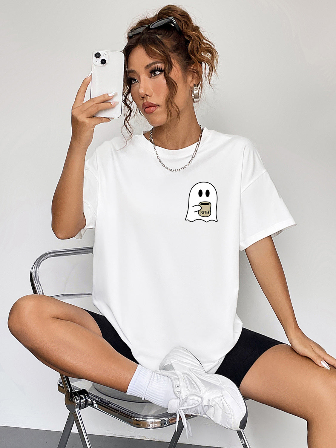 A woman wears a white round neck short sleeve ghost graphic t-shirt.
