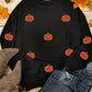 Black long-sleeve sweatshirt with sequin pumpkin appliques, styled with jeans and boots.