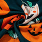 A close-up of a dark green fabric with orange pumpkin prints.