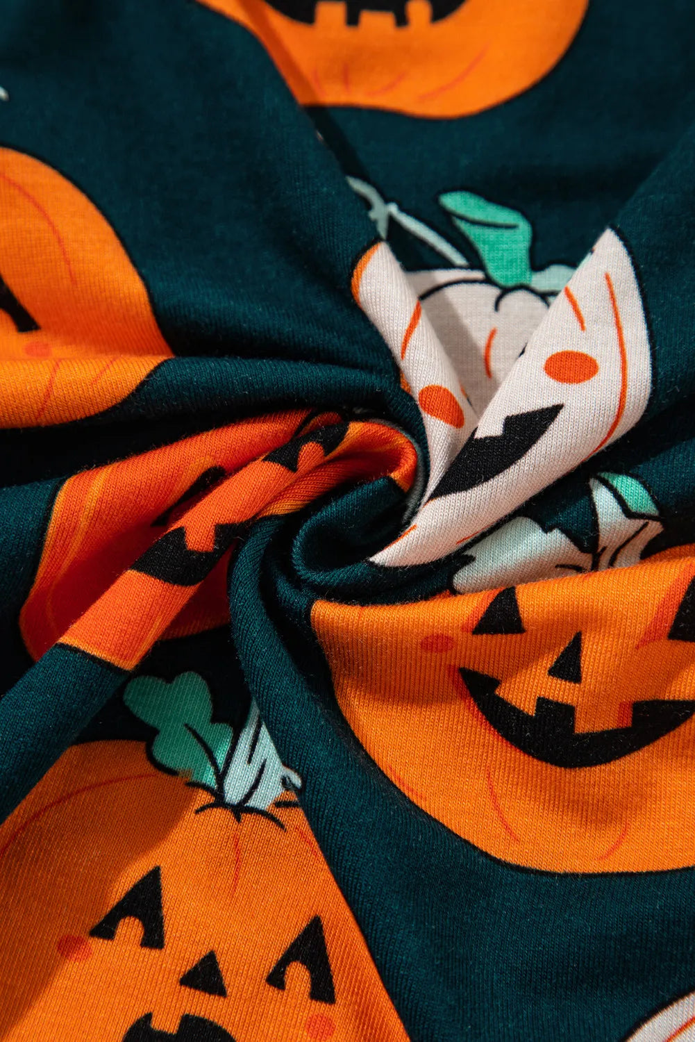 A close-up of a dark green fabric with orange pumpkin prints.