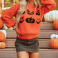 Pumpkin pattern round neck sweater in orange with a dark green mini skirt.