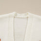 A close-up of a white knit cardigan with a pumpkin embroidered on the right side.