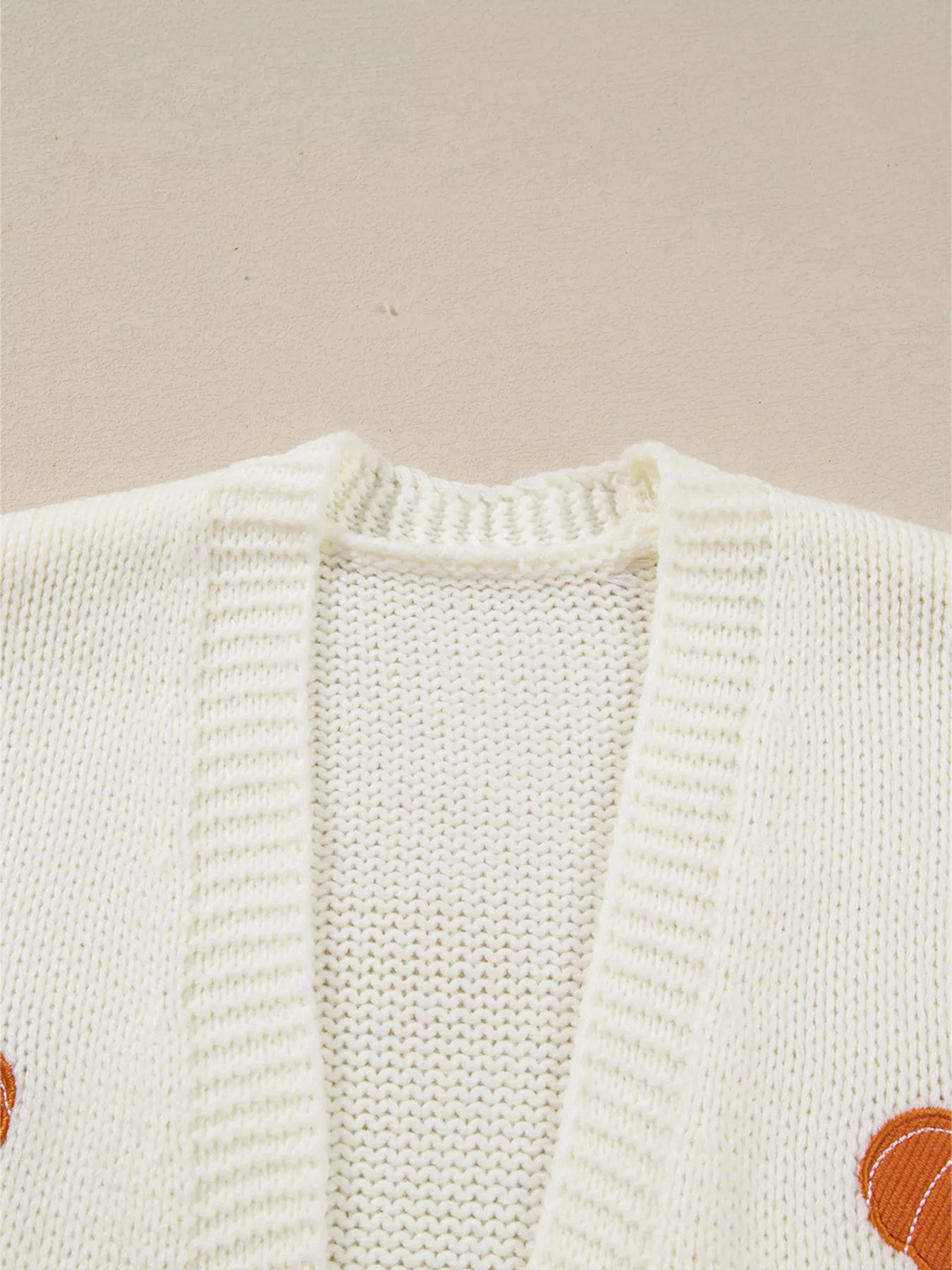A close-up of a white knit cardigan with a pumpkin embroidered on the right side.