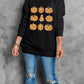 A woman wears a black long-sleeve sweatshirt with a pumpkin print and ripped jeans.