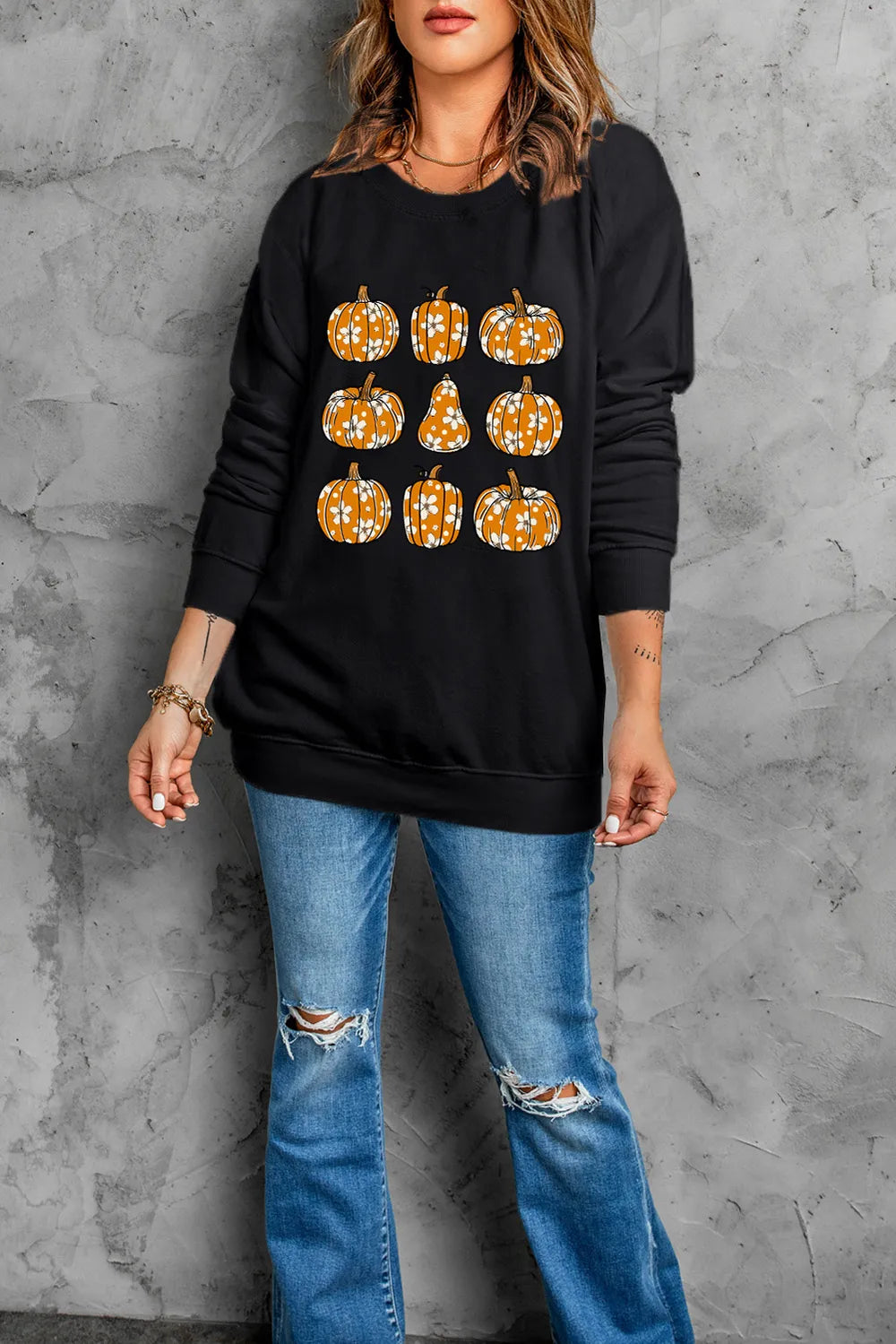 A woman wears a black long-sleeve sweatshirt with a pumpkin print and ripped jeans.