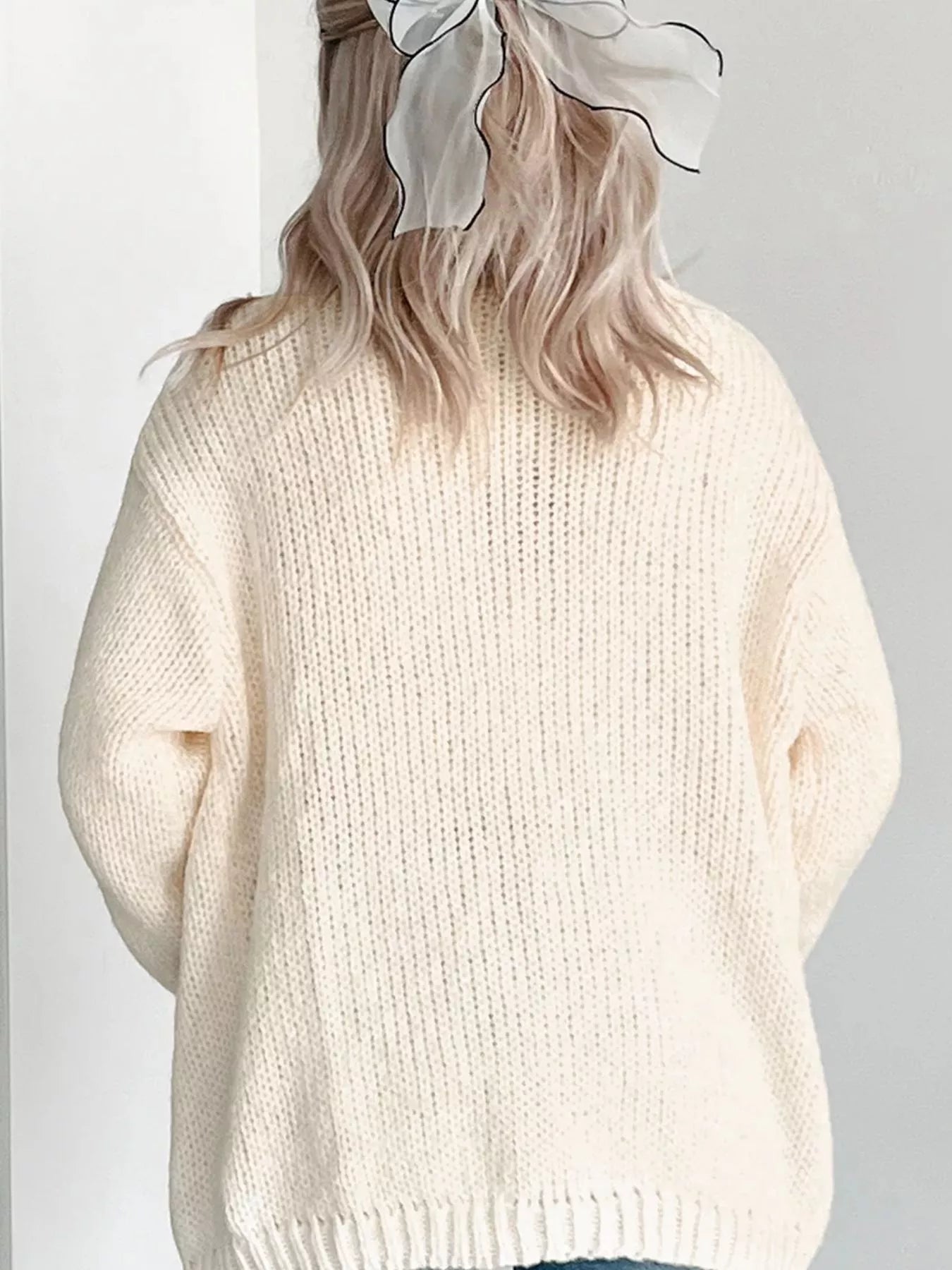 Back view of a woman wearing a cream knit cardigan with a sheer white hair bow.
