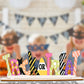 Colorful wooden "Trick or Treat" sign with blurred children and banner in the background.