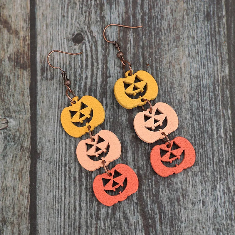 Wooden pumpkin earrings in yellow, peach, and orange hang from bronze hooks.