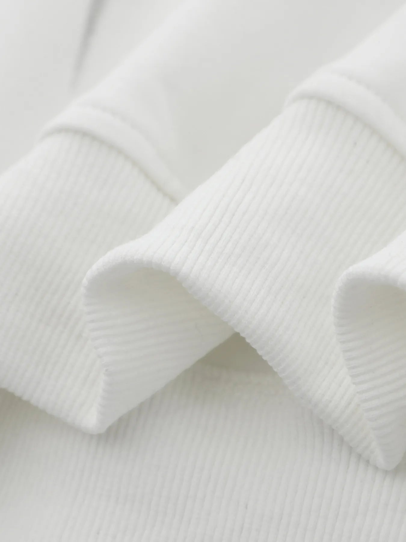 Close-up of the ribbed cuff and hem of a white oversized hoodie.