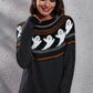 A woman smiles while wearing a black ghost pattern round neck long sleeve sweater.