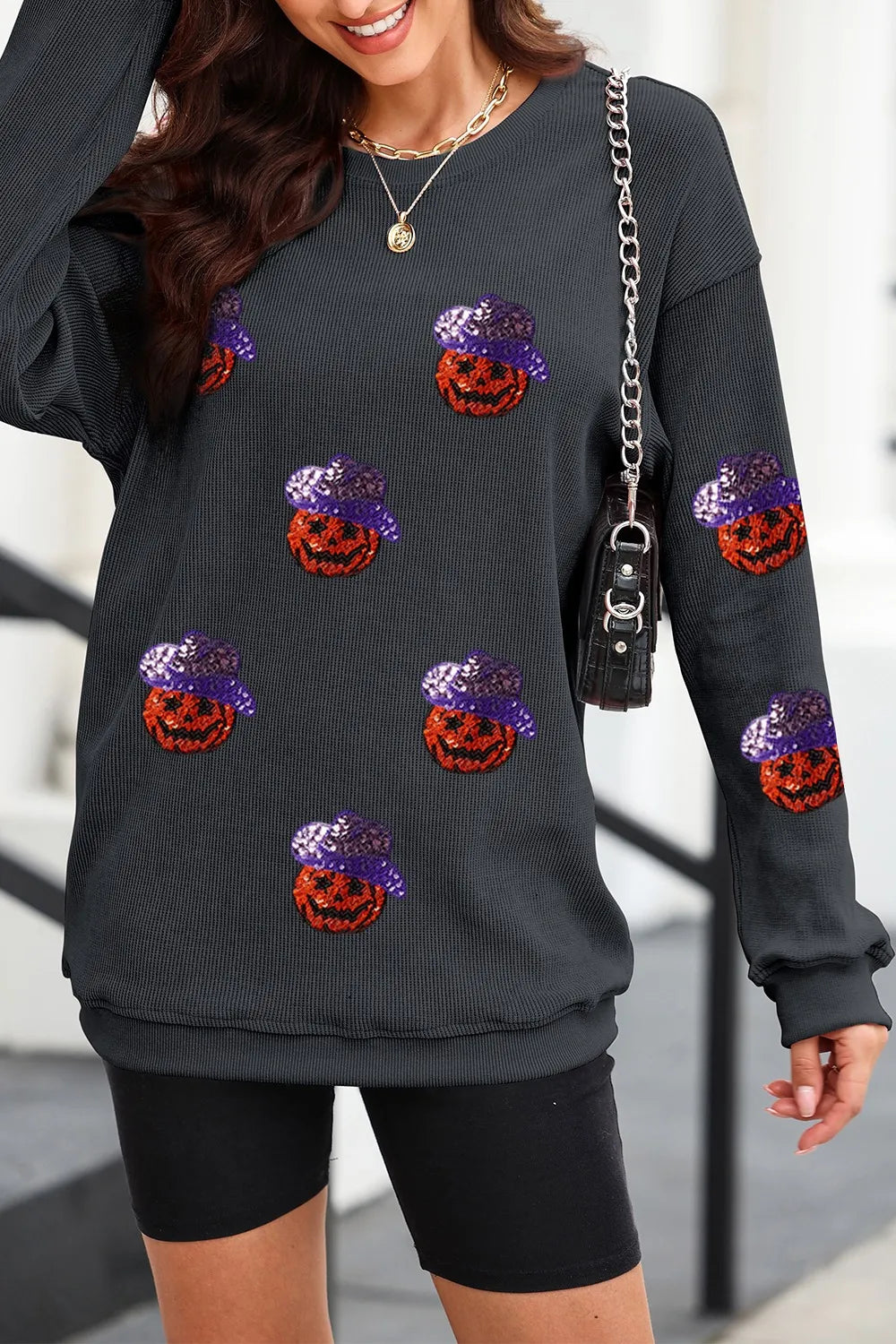 A woman wears a black long-sleeve sweatshirt with sequin pumpkins and black shorts.