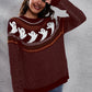A woman smiles, shielding her eyes, wearing a maroon ghost pattern sweater and jeans.