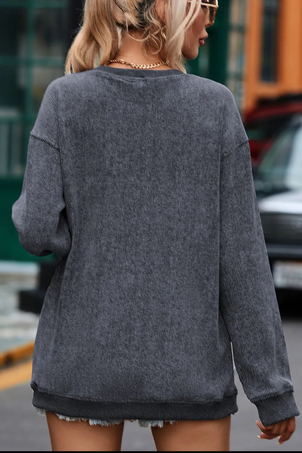A woman from behind wears a gray long-sleeve sweatshirt with a ribbed texture.