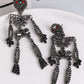 Skeleton-shaped dangle earrings adorned with dark glass stones and red eyes.