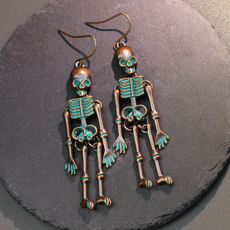 Two antique bronze skeleton alloy earrings with teal accents hang on a dark surface.