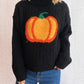 Black cable-knit turtleneck sweater with an orange pumpkin applique.