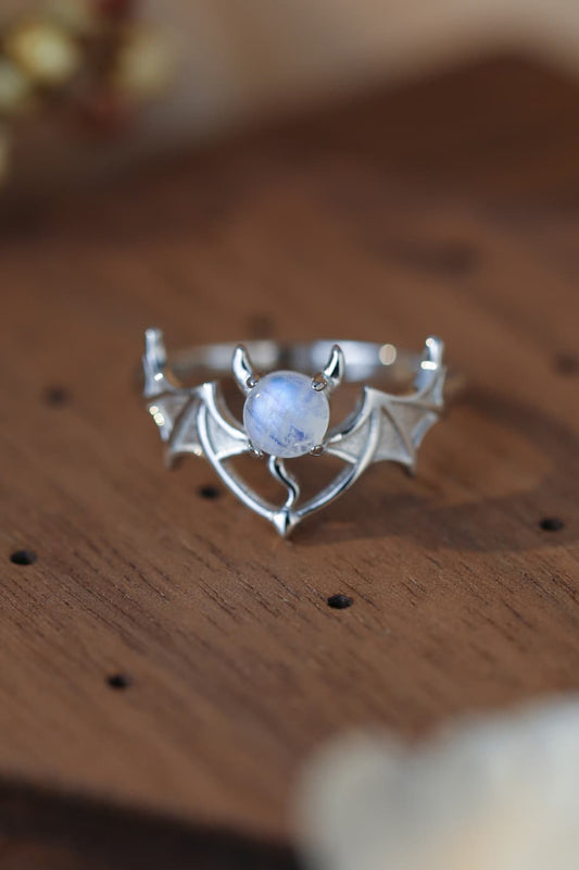 Sterling silver bat ring with a round moonstone on a wooden surface.