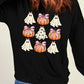 A woman wears a black sweatshirt with a pumpkin and ghost pattern.