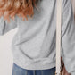 A woman from behind wears a gray sweatshirt and blue jeans, with a white bag.