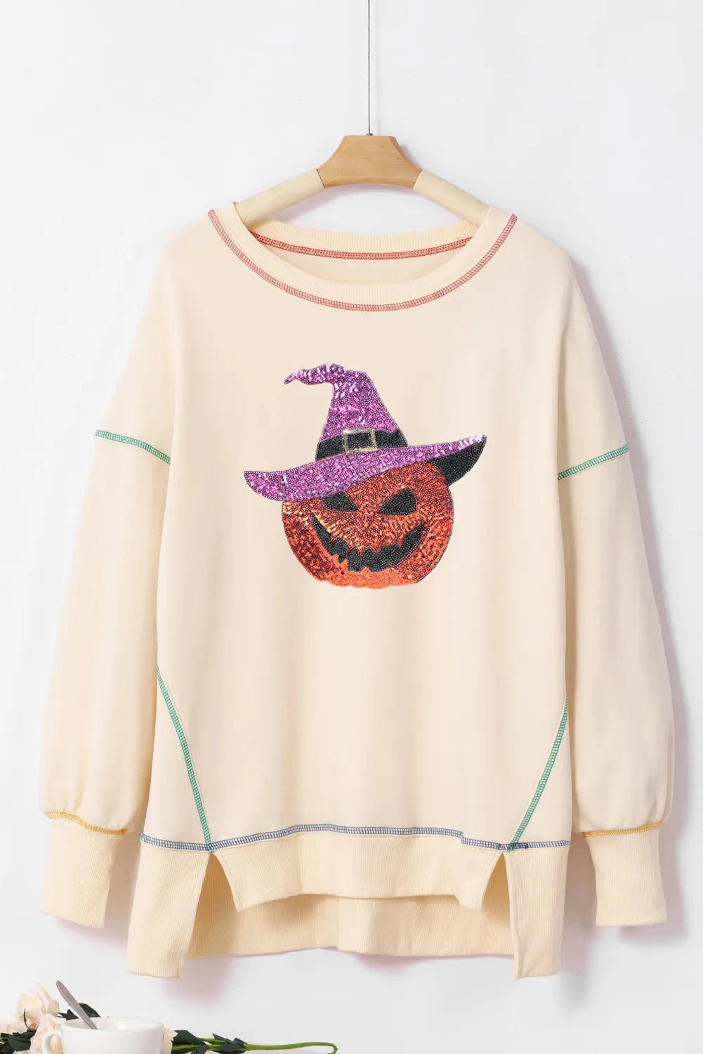 Cream sweatshirt with a sequin pumpkin wearing a witch hat and contrast stitching.