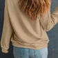 A woman from behind wears a beige drop shoulder sweatshirt and blue jeans.