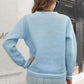 A woman from behind wears a light blue pullover sweater with white stripes.