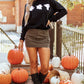 A woman wears a black long-sleeve sweatshirt with three white ghost graphics.