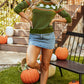 A woman wears a green ghost-patterned sweater with a denim skirt and boots.