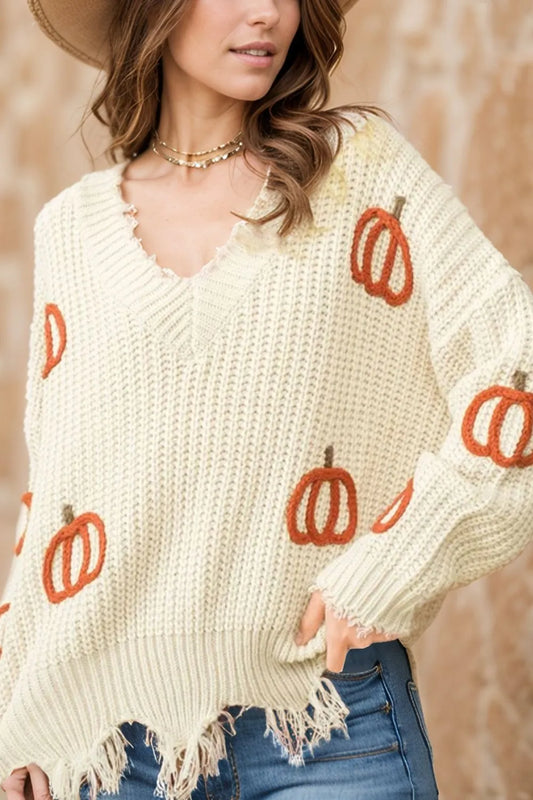 A woman wears a cream-colored, long-sleeve, V-neck sweater with pumpkin designs and a raw hem.